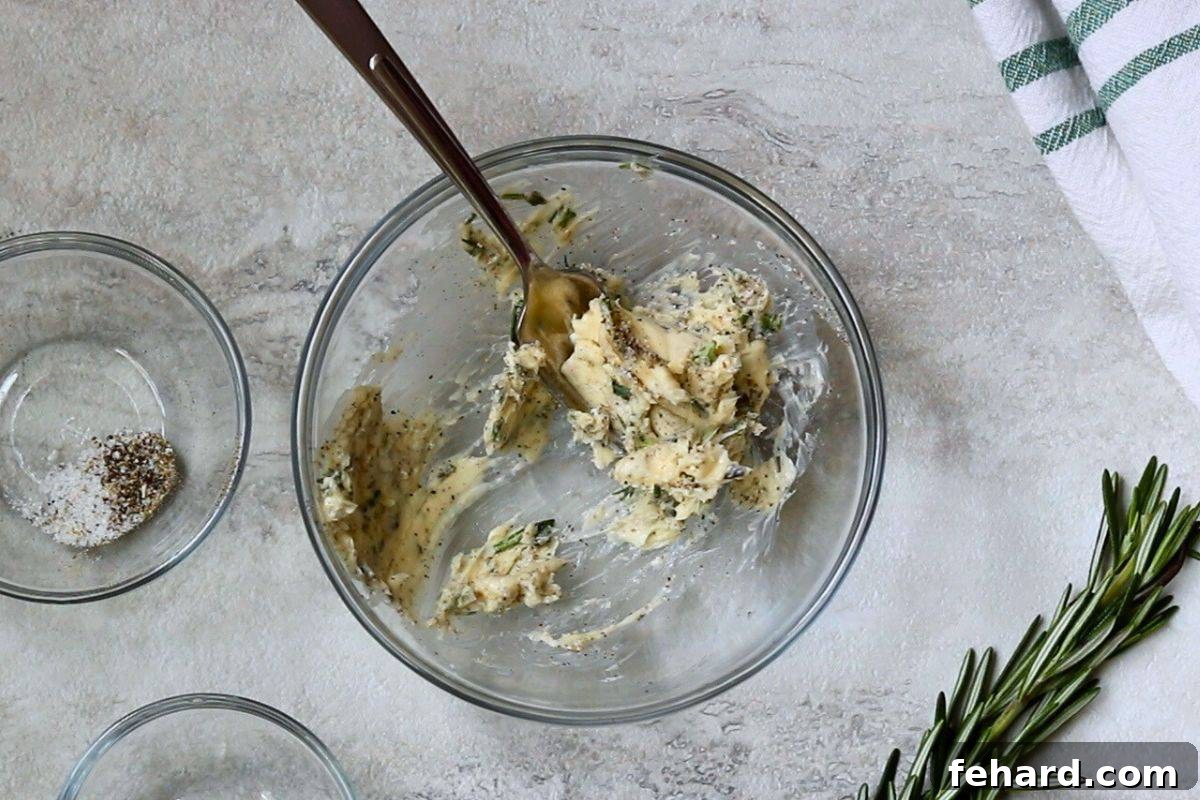 Compound butter with fresh herbs, lemon zest, salt, and pepper mixed in a small bowl with a fork, next to fresh rosemary sprigs.