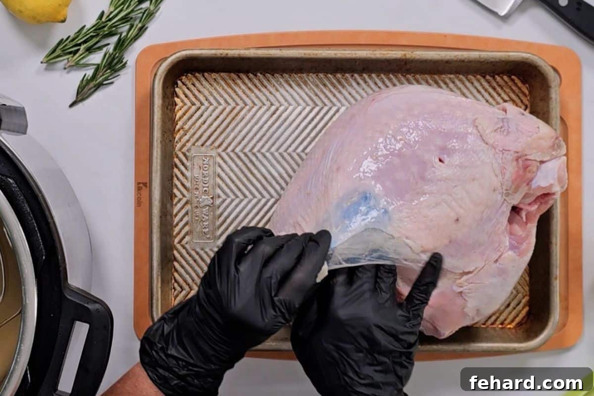 Gloved hand applying compound butter under the skin of a raw turkey breast on a cutting board.