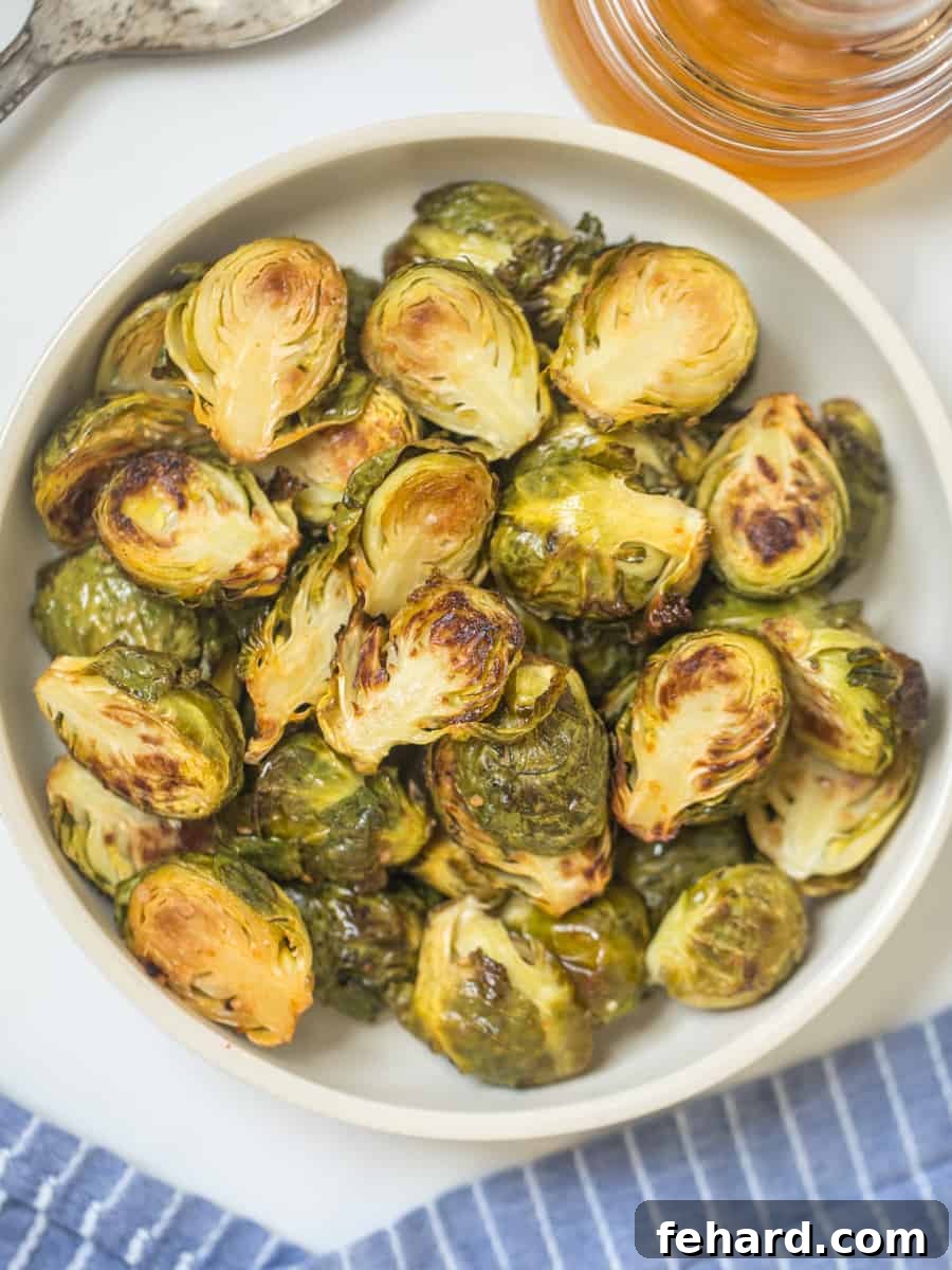 Roasted Brussels sprouts in serving bowl with honey jar in background, showcasing a perfect glaze.