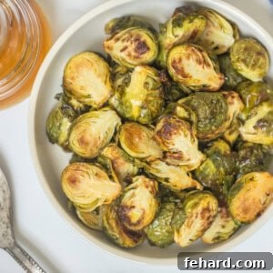 Roasted Brussels sprouts in serving bowl with honey jar in background.