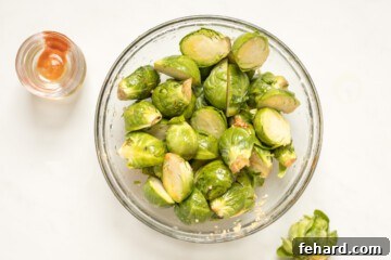 Halved Brussels Sprouts in mixing bowl with garlic, honey, olive oil, and hot sauce.