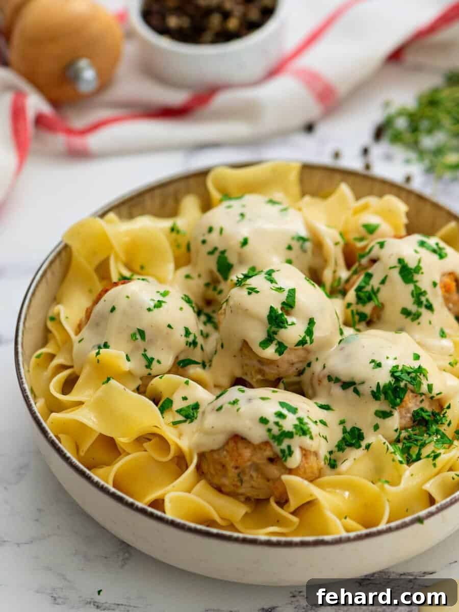 A bowl of delectable Turkey Swedish Meatballs served over golden egg noodles, generously topped with fresh parsley and a rich, creamy sauce.