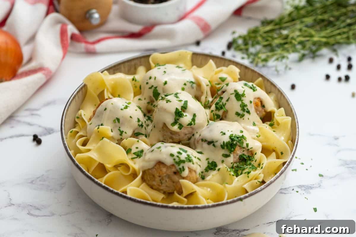 A beautifully presented bowl of turkey Swedish meatballs, generously covered in creamy sauce, served over egg noodles and garnished with fresh parsley.