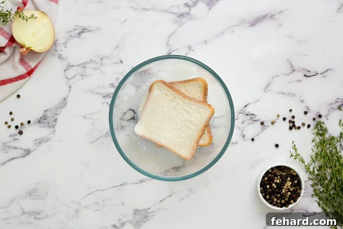 Slices of sandwich bread actively soaking in milk within a mixing bowl, ready for meatball preparation.