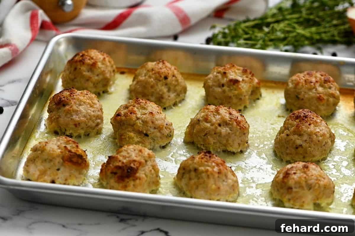 Freshly baked turkey meatballs, golden brown and perfectly cooked, resting on a rimmed baking sheet after being removed from the oven.