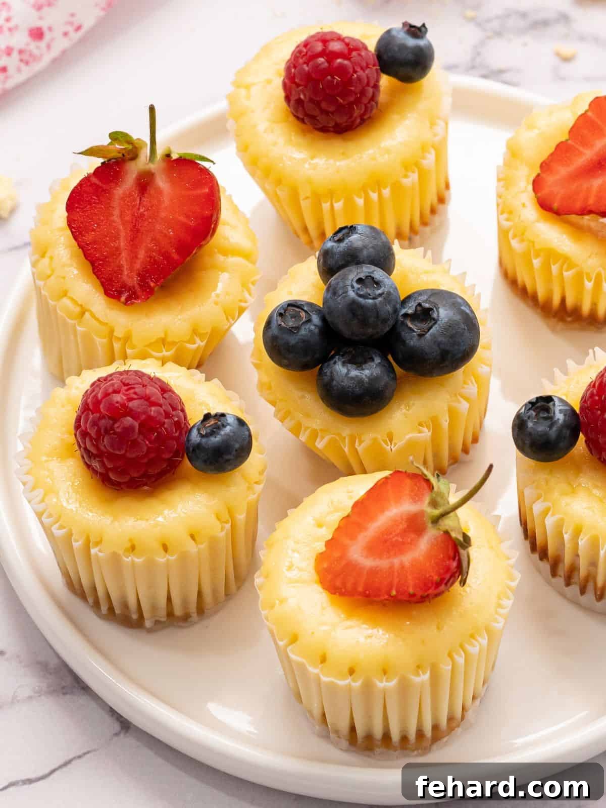 A plate of perfectly portioned mini cheesecakes, elegantly topped with a vibrant medley of fresh berries and a sprig of mint, ready to be enjoyed.