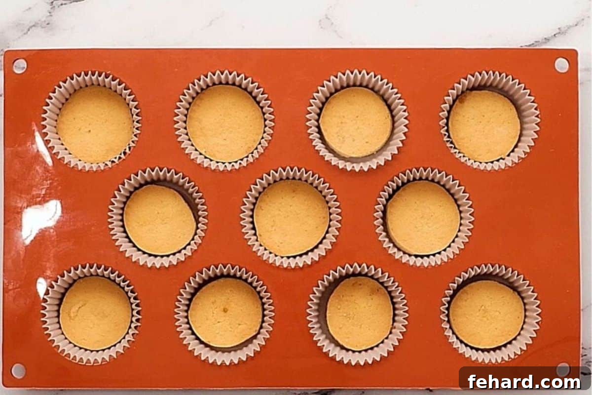 A mini muffin tin lined with mini cupcake liners, each containing a single mini vanilla wafer, ready for the cheesecake batter.