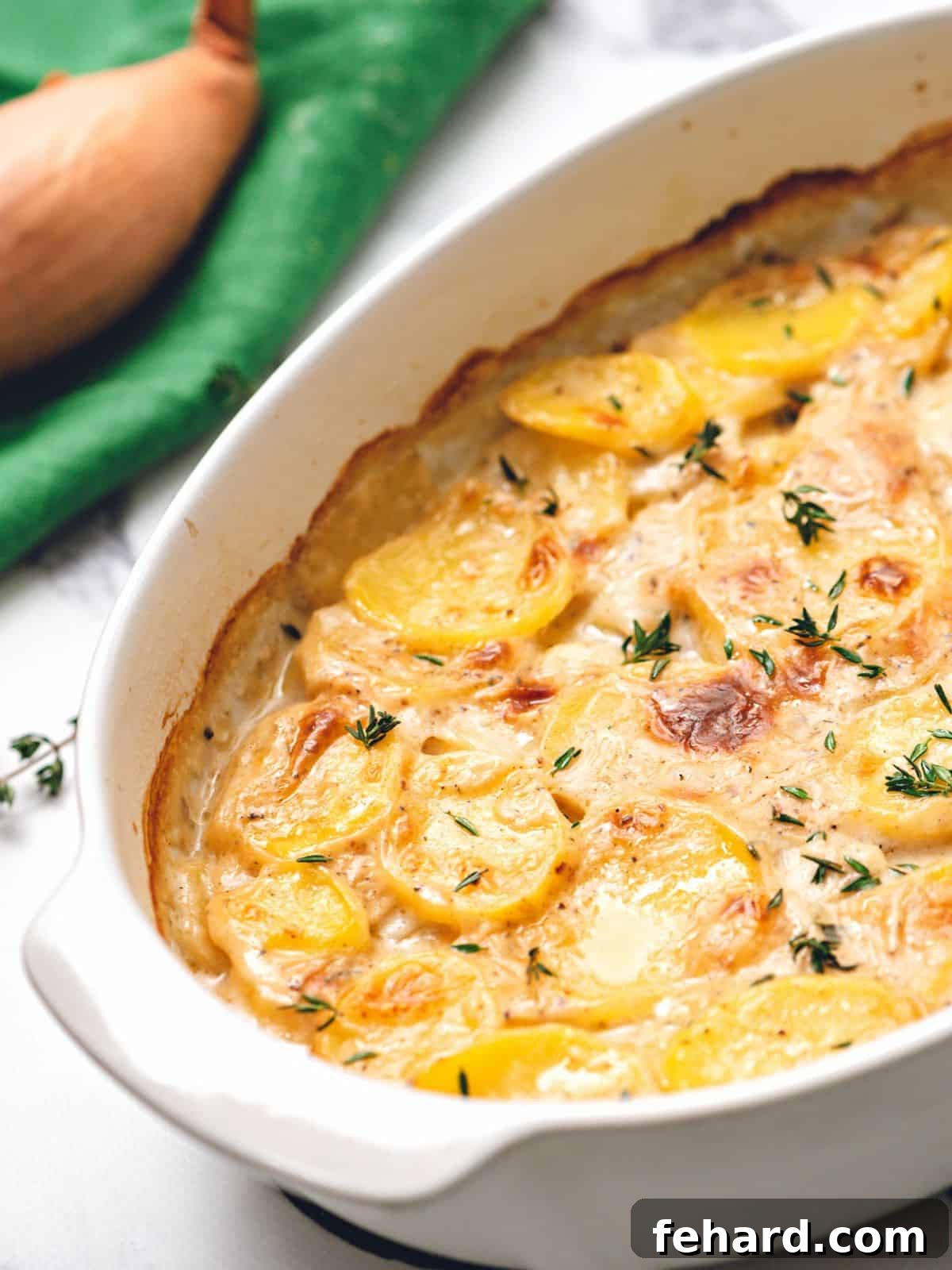 Scalloped Potatoes Baked Scalloped Potatoes in White baking dish topped with fresh thyme.