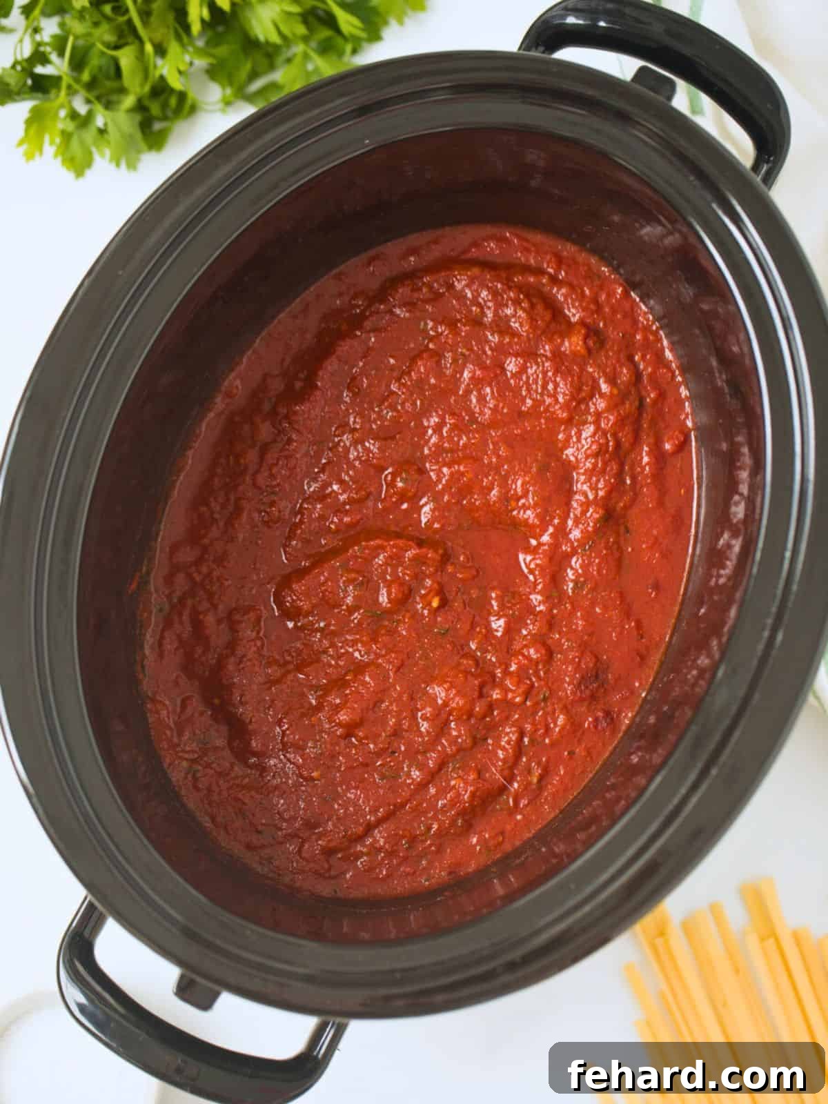 Slow Cooker Spaghetti Sauce Spaghetti sauce made with crushed canned tomatoes and pantry staples inside slow cooker next to parsley and pasta.