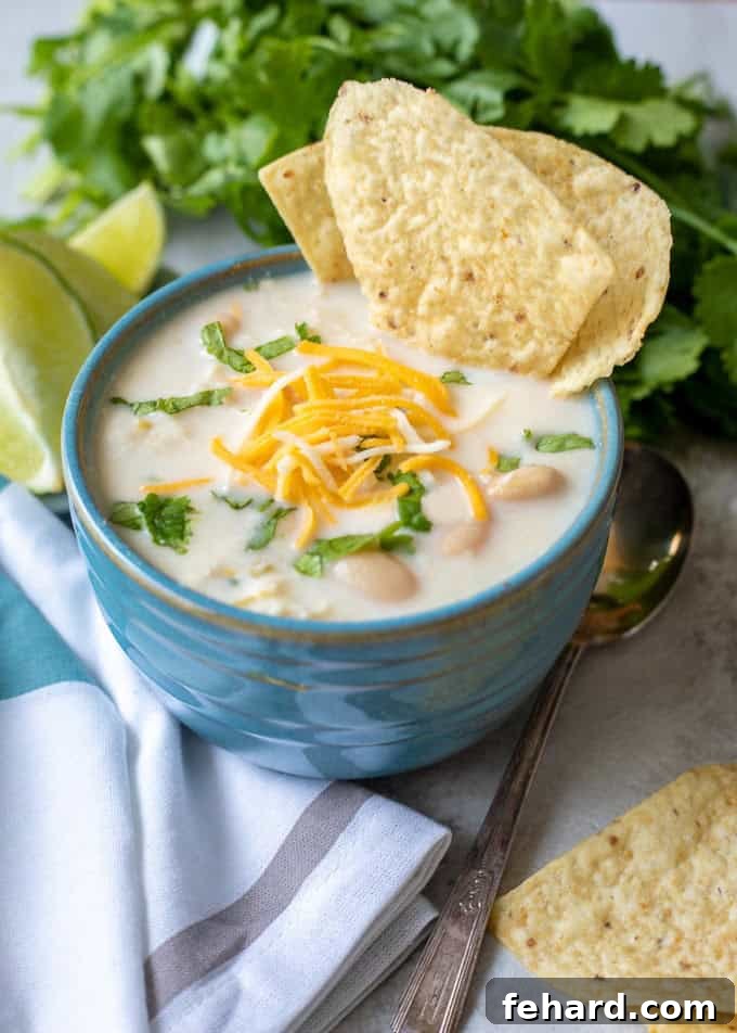 Instant Pot White Chicken Chili Recipe Bowl of Instant Pot White Chicken Chili in blue bowl topped with shredded cheese, minced cilantro and served with lime wedges and tortilla chips on the side.