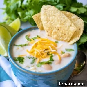 Bowl of Instant Pot White Chicken Chili in blue bowl topped with shredded cheese, minced cilantro and served with lime wedges and tortilla chips on the side.