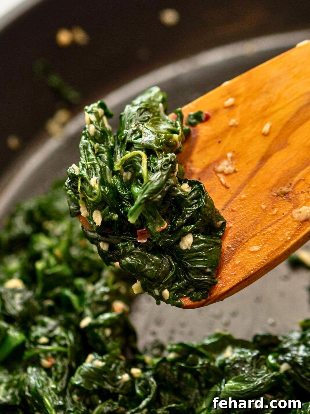 Sauteed wilted spinach on wooden spoon showing lemon and garlic in sauteed spinach.