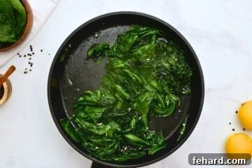 Fresh spinach in saute pan with lemons to side showing the spinach beginning to wilt.