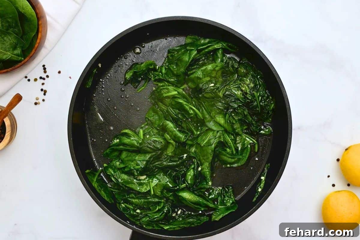 Fresh spinach in saute pan with lemons to side showing the spinach beginning to wilt.