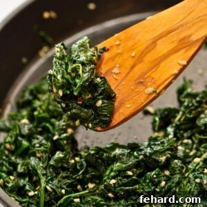 Wooden spoon scooping up sauteed spinach with lemon and garlic from saute pan.