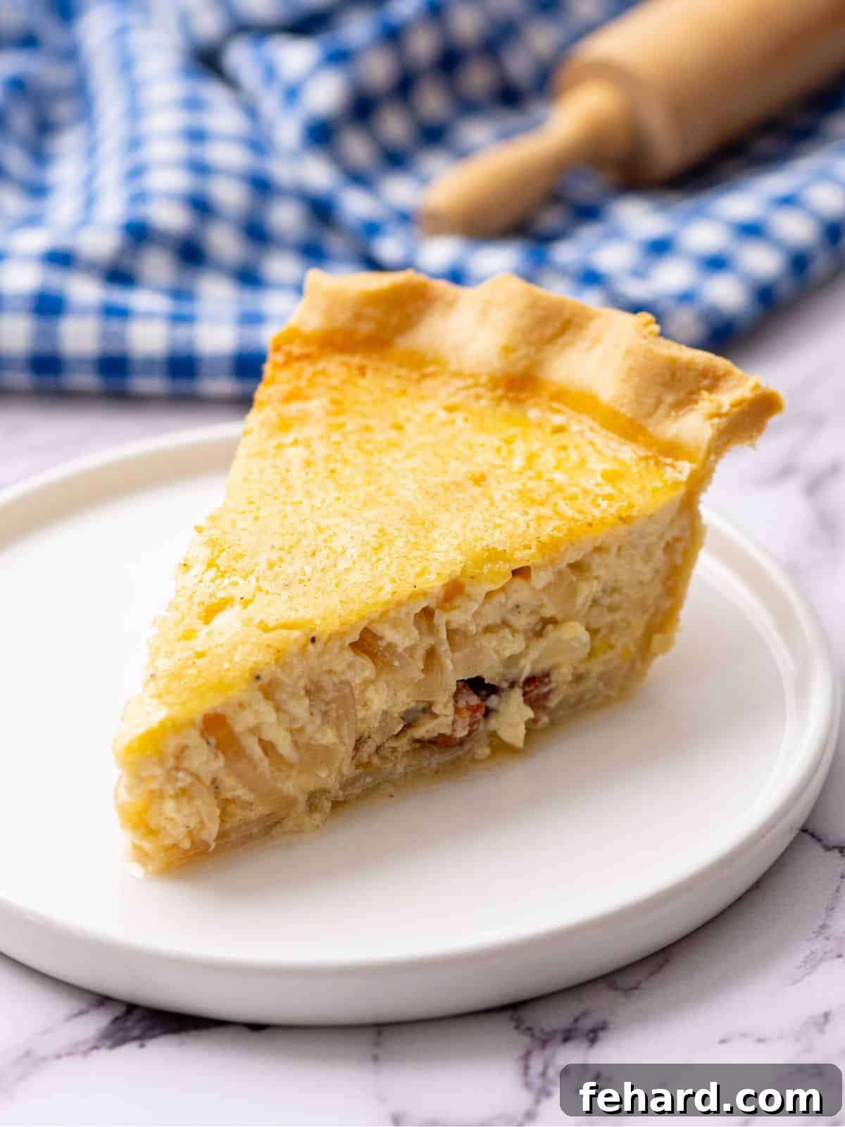 Slice of classic French Quiche Lorraine on white plate, showcasing crispy bacon, melted Swiss cheese, and golden-brown caramelized onions in a flaky crust.