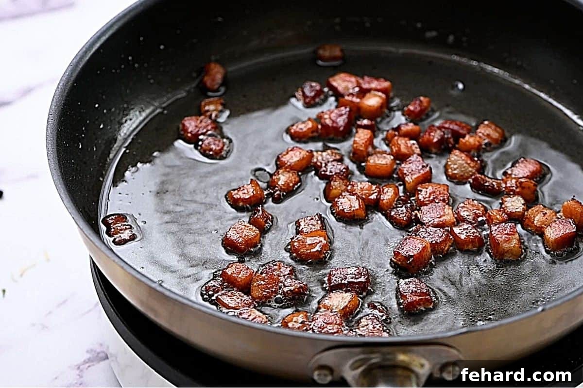 Crispy rendered bacon in a skillet, showcasing the golden-brown bits and melted fat.