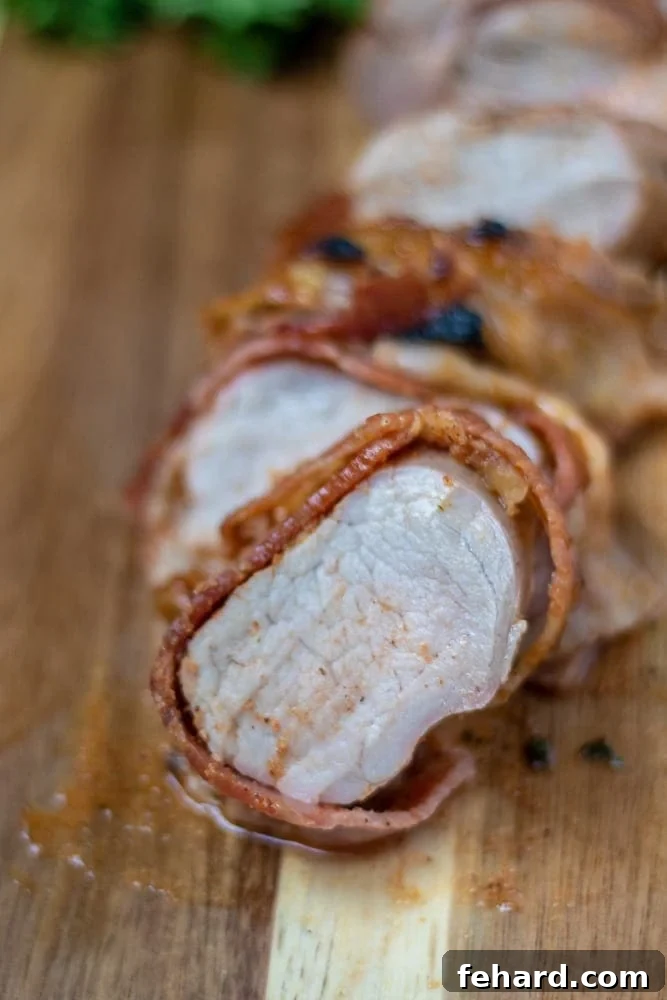 Bacon Wrapped Pork Tenderloin sliced on wooden cutting board, showcasing its juicy interior and crispy bacon crust.