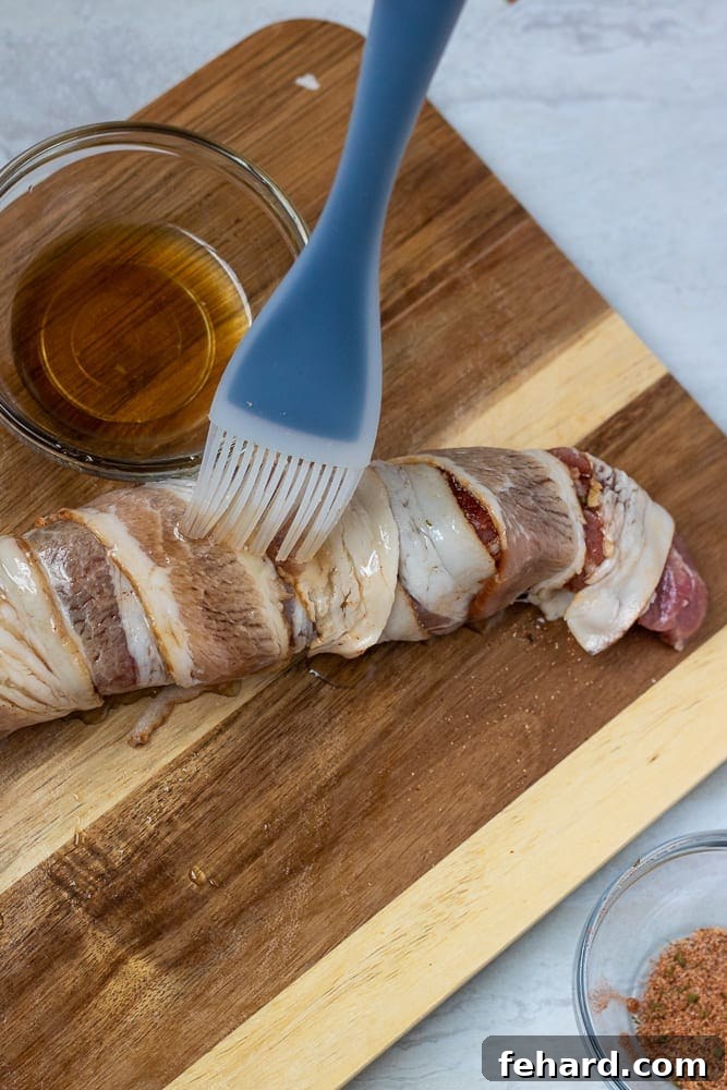 Brushing maple syrup over bacon wrapped tenderloin, showing the glaze being applied.