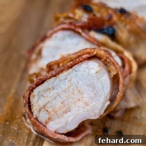 Bacon Wrapped Pork Tenderloin sliced on wooden cutting board, showing a close-up of juicy pork tenderloin wrapped with crispy bacon.