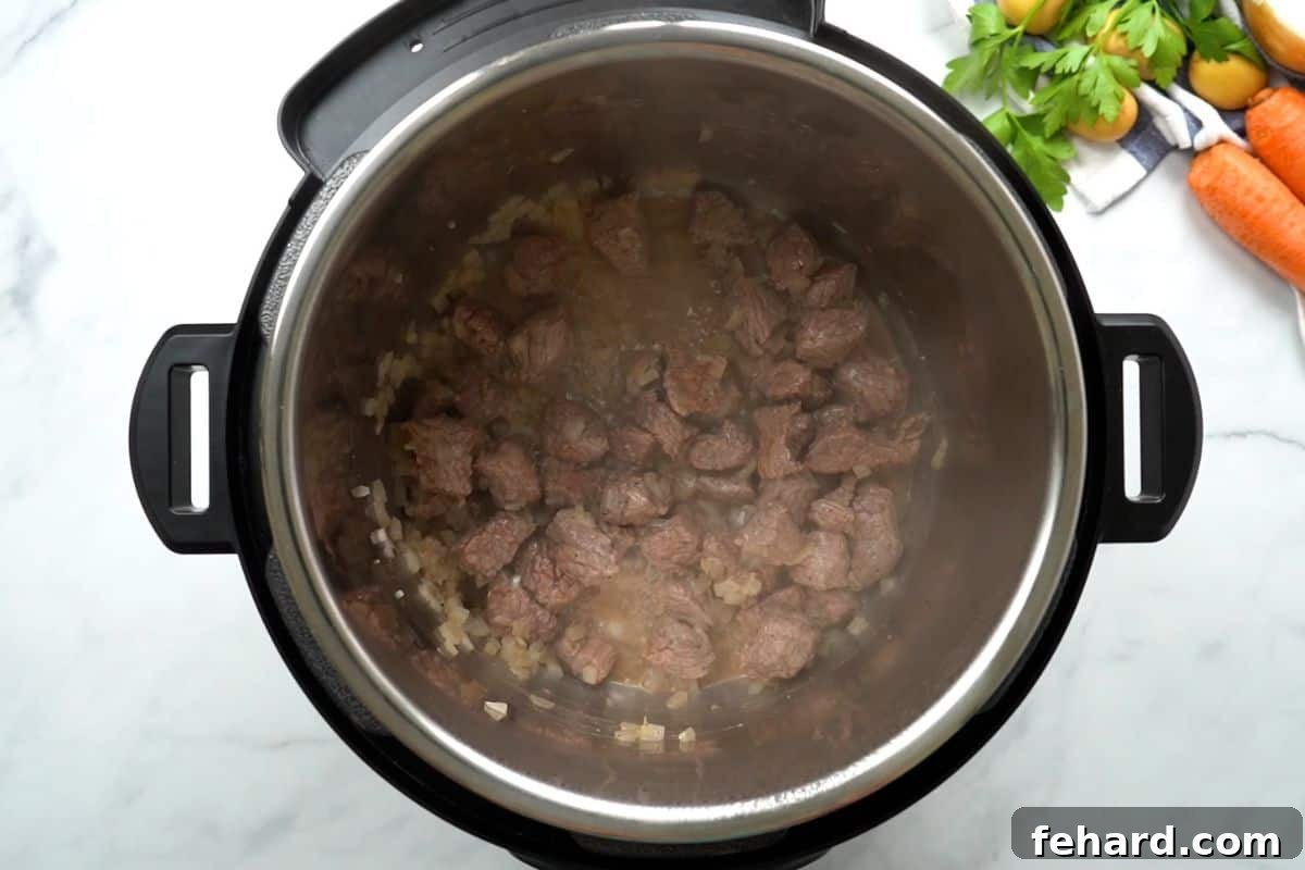 Chunks of beef stew meat and minced onion searing in the Instant Pot's inner pot, developing a rich brown color.
