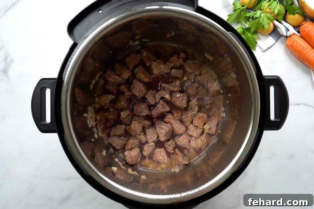 Red wine being poured into the Instant Pot with seared beef, and a wooden spoon scraping the bottom to deglaze the pot.