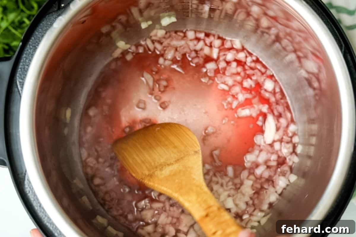 Spaghetti Sauce Instant Pot Recipe A wooden spoon scraping up browned bits from the bottom of an Instant Pot inner pot after adding liquid.