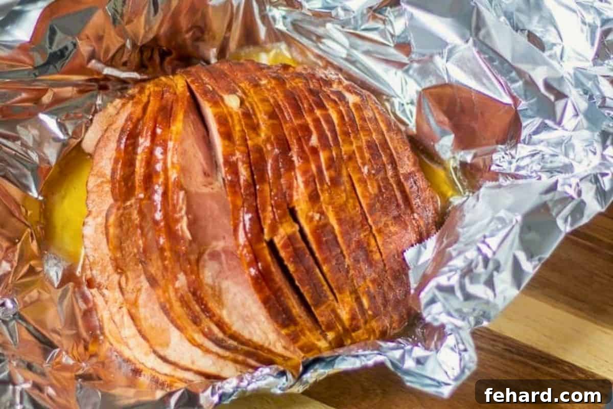 Instant Pot Honey Baked Ham Glazing Process Spiral sliced ham positioned on heavy-duty foil with a generous amount of sweet pineapple glaze being poured over its surface.