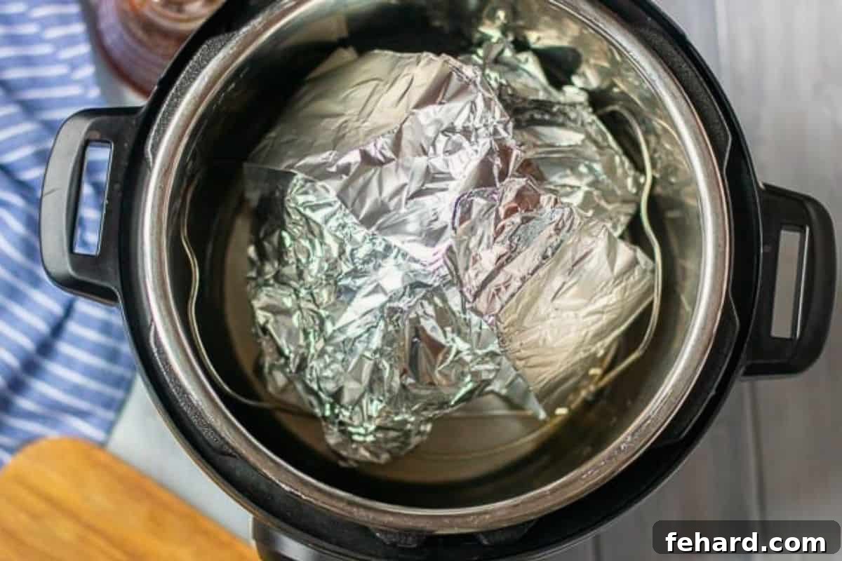 Instant Pot Ham Recipe in Pressure Cooker Honey Glazed Ham, wrapped snugly in foil, resting on a trivet inside an Instant Pot pressure cooker, ready for cooking.