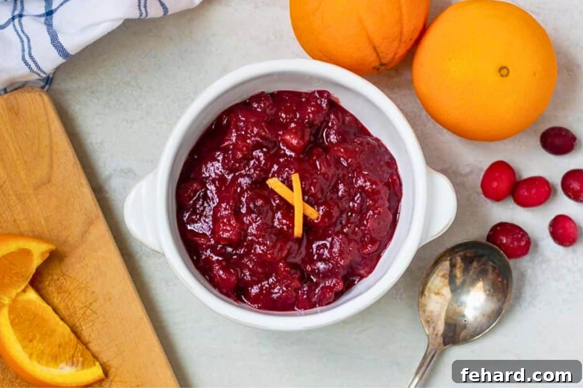 Easy Cranberry Orange Sauce beautifully dished out in a white serving bowl, garnished with fresh orange zest and whole cranberries in the background.