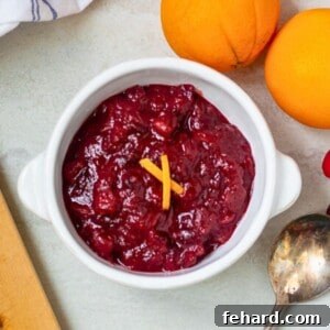 Homemade Cranberry Orange Sauce served in a white dish, garnished with orange zest and fresh cranberries in the background.