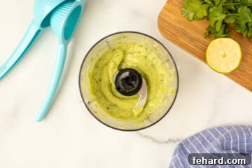 Blended avocado lime sauce in small food processor next to citrus juicer.