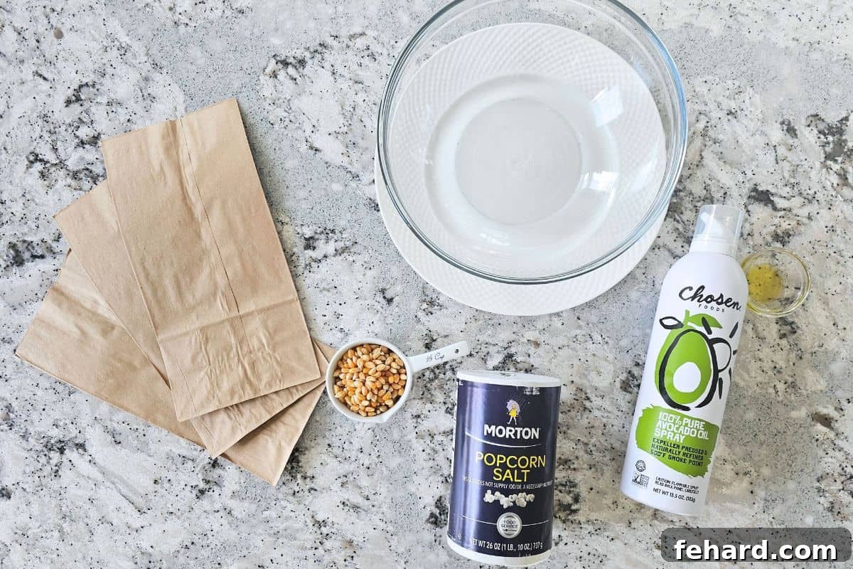 Ingredients for making microwave popcorn at home on counter: heat-safe bowl, brown lunch bags, popcorn salt, cooking spray, various oils, and popcorn kernels.