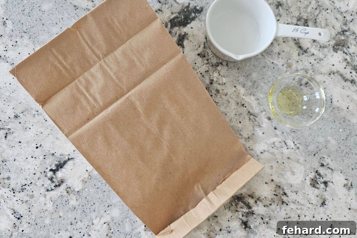 Brown paper bag folded over with popcorn kernels inside, ready for microwave popping, with oil on the side.
