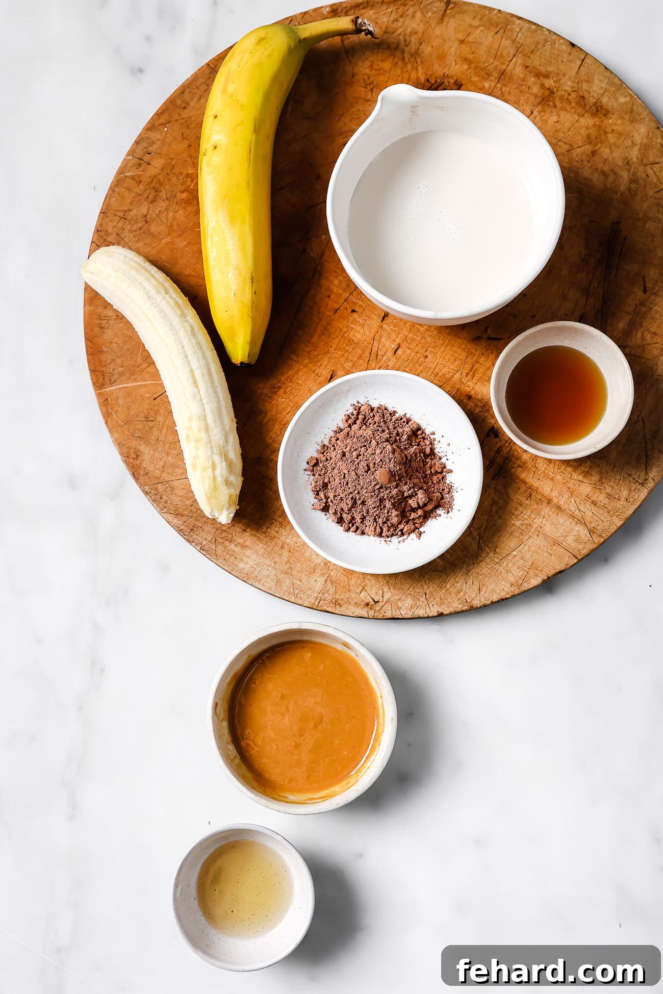 Pre-measured ingredients for the chocolate peanut butter smoothie arranged neatly on a wooden cutting board against a white countertop.