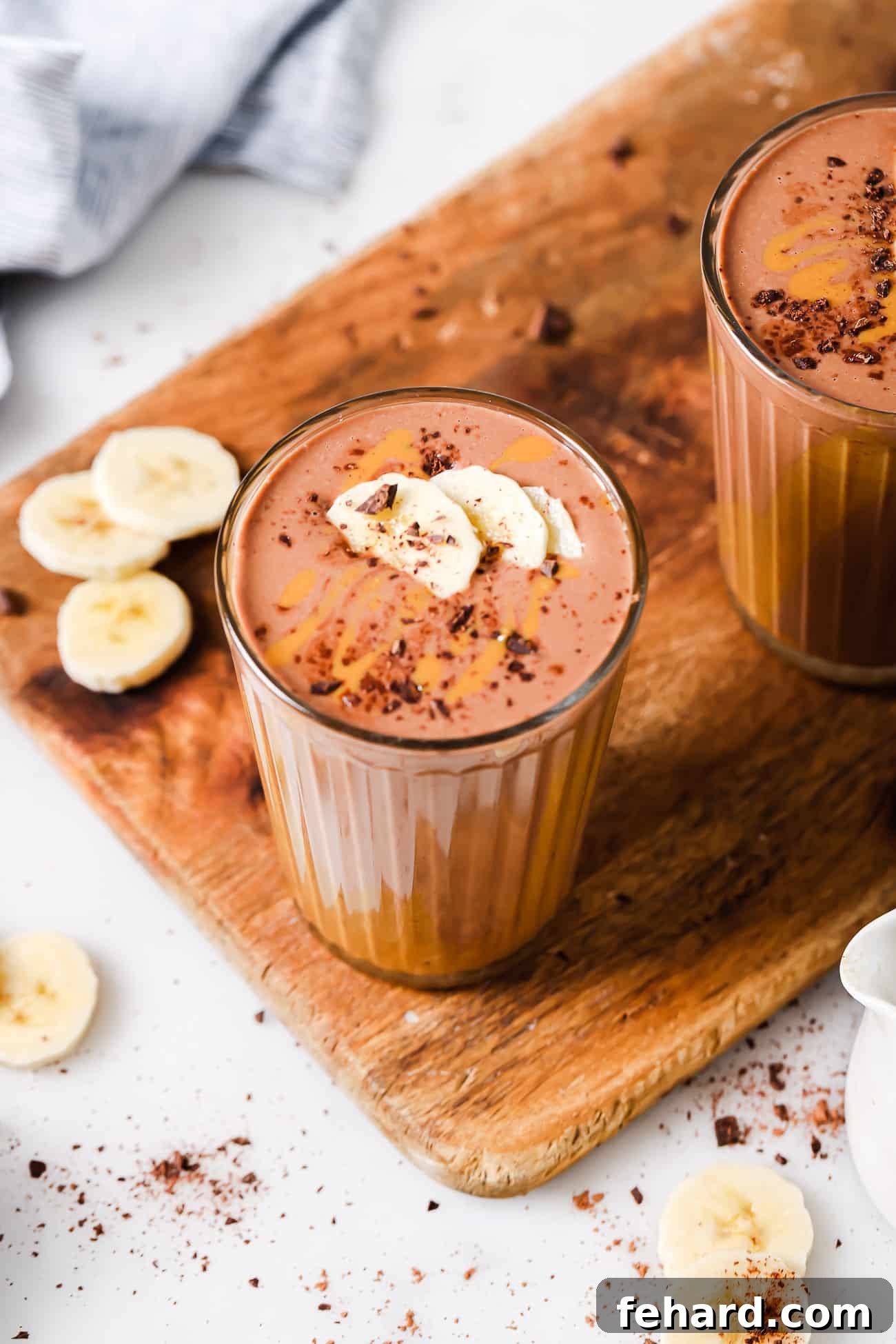 A tall glass of peanut butter chocolate smoothie garnished with banana slices and a light dusting of cocoa powder.