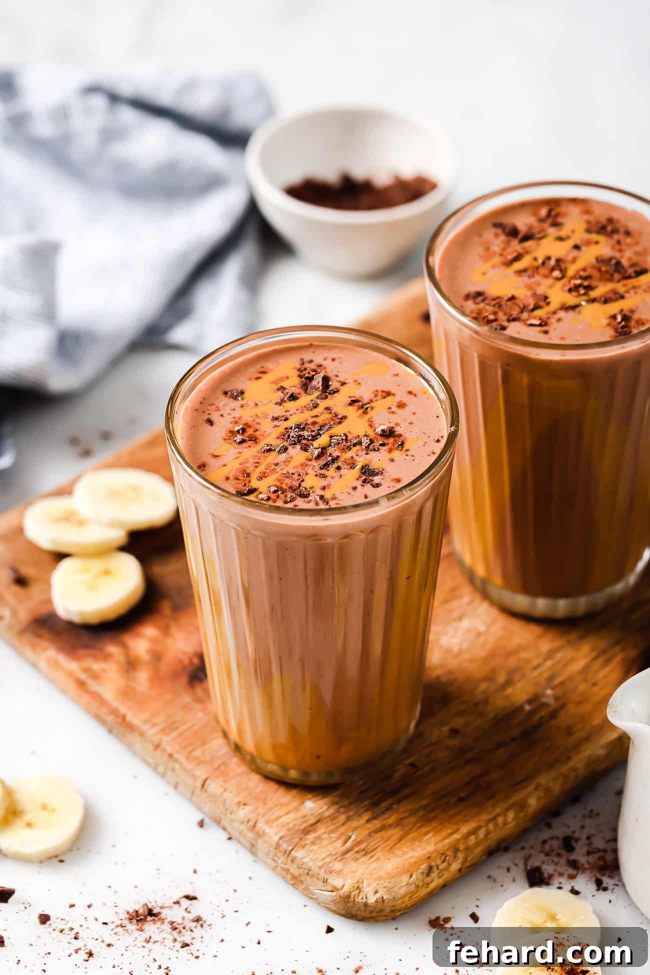 Two glasses of rich chocolate peanut butter smoothie, artfully arranged on a wooden cutting board, ready to be enjoyed.