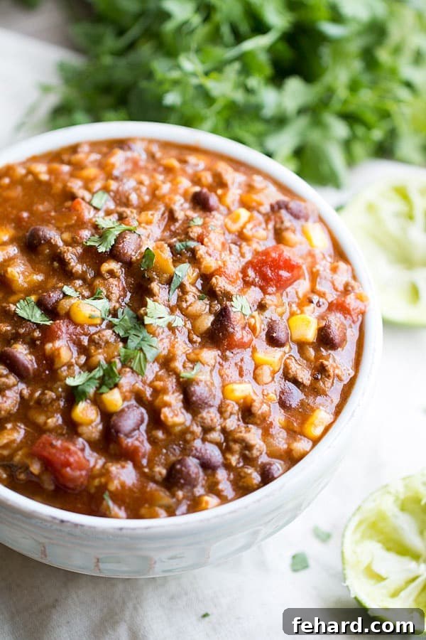 Slow Cooker Tex Mex Soup in a bowl, topped with shredded cheese and tortilla strips.