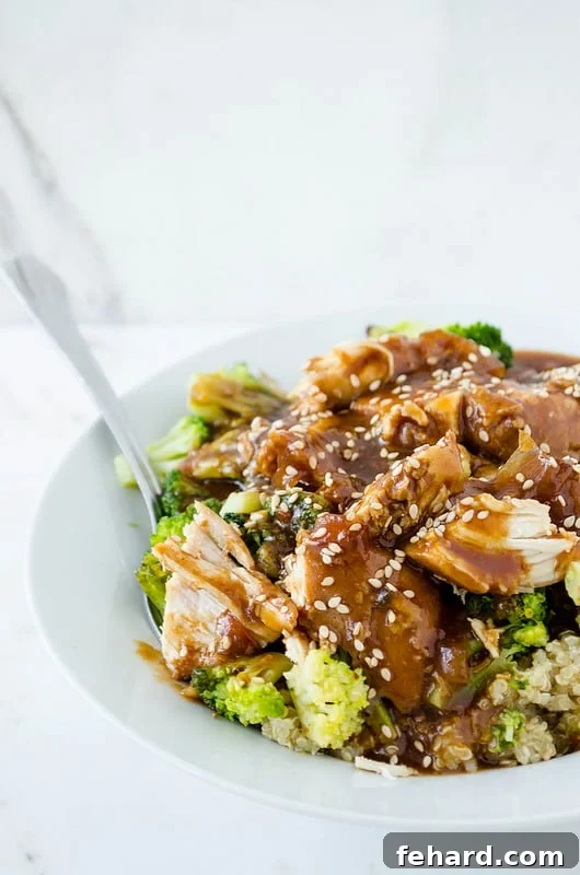 slow cooker sesame garlic chicken served over rice, garnished with sesame seeds and green onions.