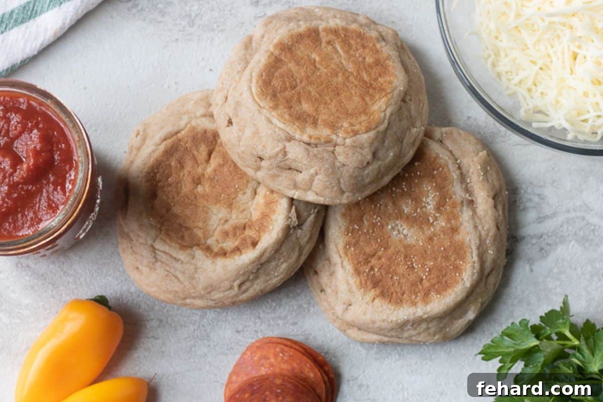 English muffins, a jar of pizza sauce, and a block of shredded mozzarella cheese on a kitchen counter.