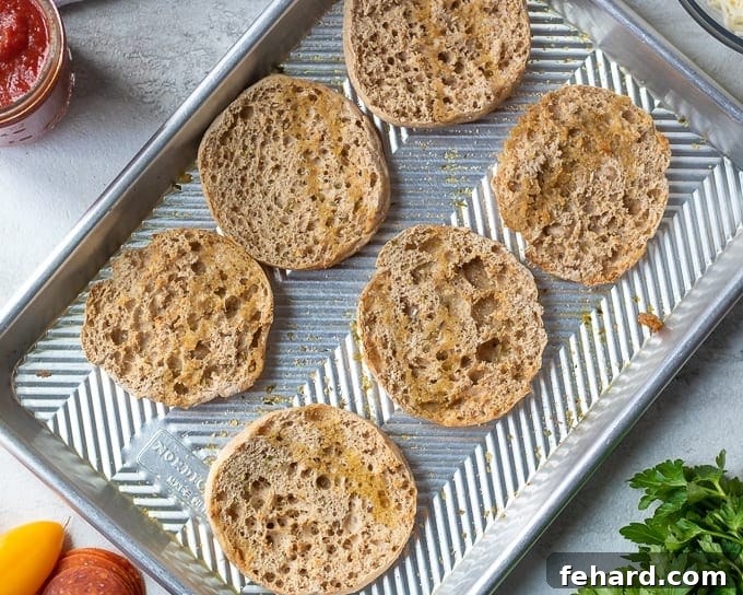 Tray of English Muffin Halves brushed with garlic oil, ready for topping.