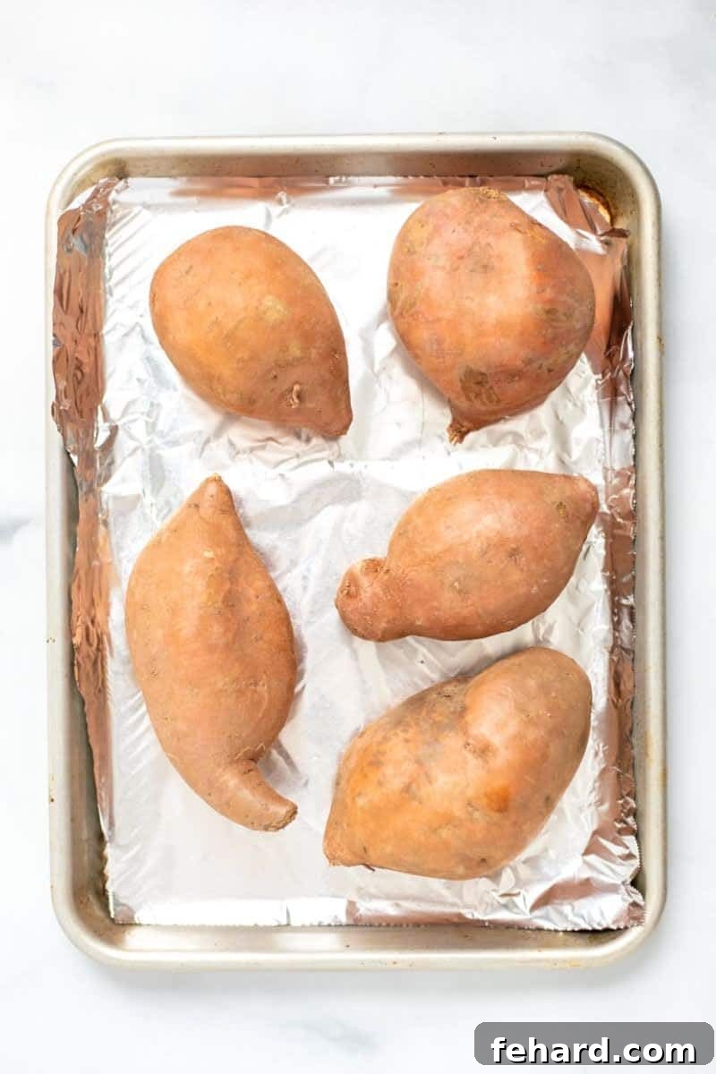 Sweet Potato Baking Preparation Several raw sweet potatoes expertly placed on a foil-lined baking sheet, prepared and ready for baking in the oven. A visual guide to easy sweet potato preparation.