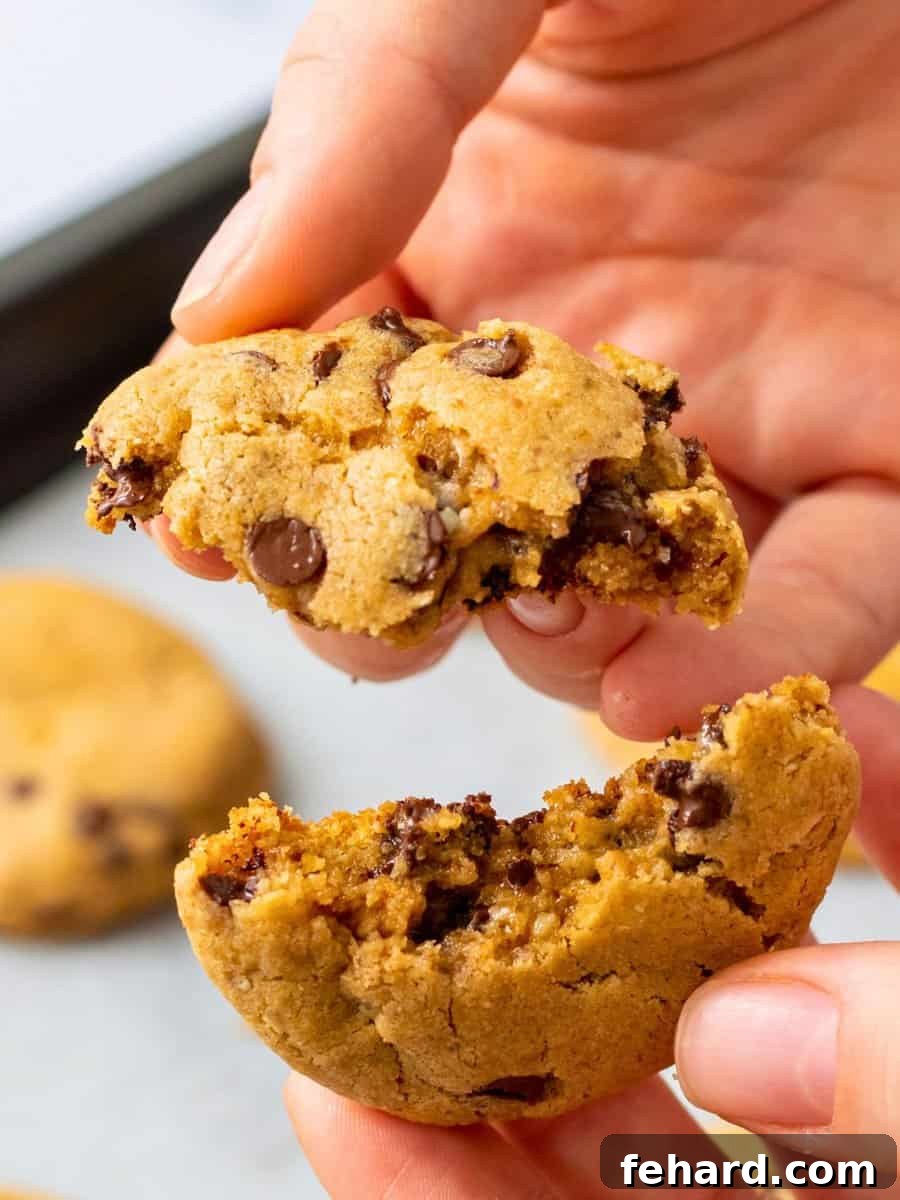 Authentic Neiman Marcus Cookies A gooey warm baked Neiman Marcus cookie being broken in half to reveal pools of melted chocolate, highlighting its irresistible texture.