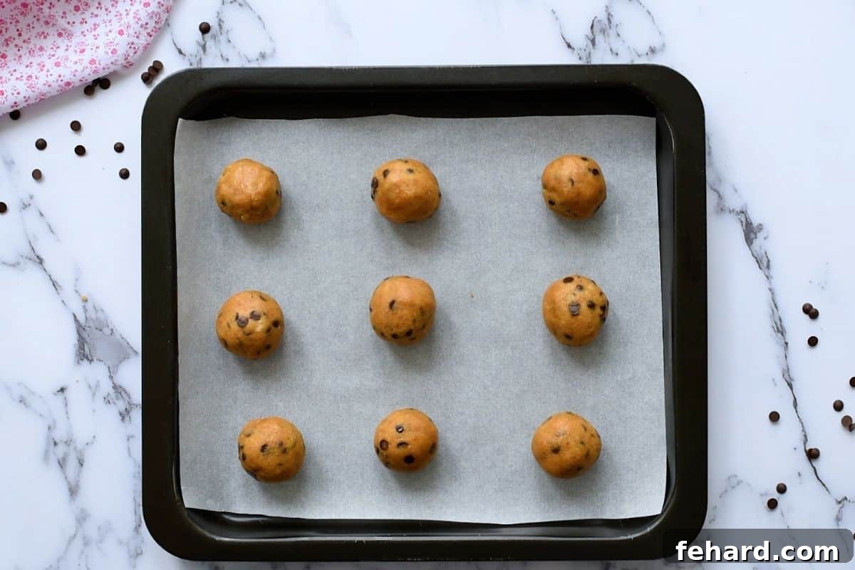 Neiman Marcus Chocolate Chip Cookies Ready to Bake 9 rolled cookie dough balls neatly arranged on a parchment-lined baking sheet, spaced for optimal baking.