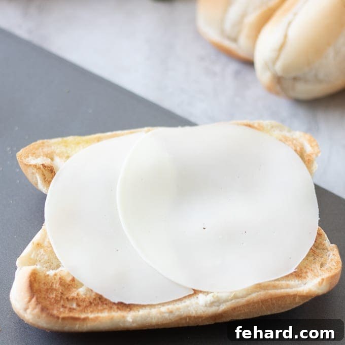 Meatball Sub Sandwich preparation: Adding cheese to bun Provolone Cheese Slices neatly arranged on a toasted hoagie bun.