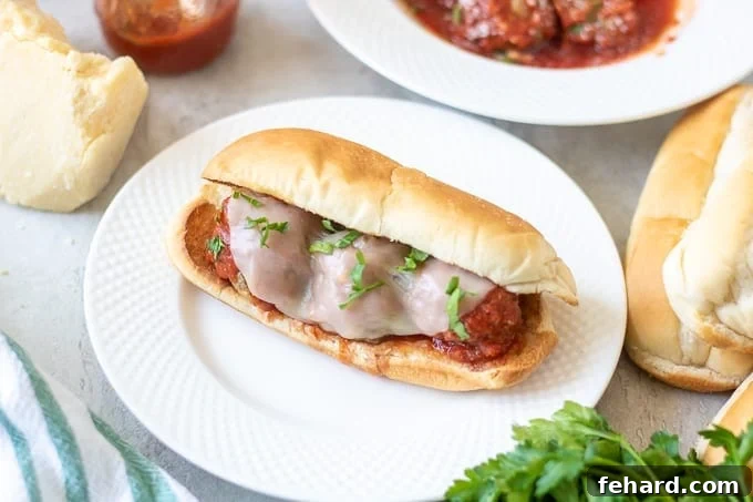 Easy Meatball Sub Sandwiches: Ready to serve Completed Meatball Sub on a white plate with sauce and cheese in the background.