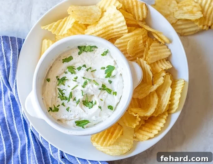Serving Ideas for French Onion Chip Dip A bowl of homemade French onion chip dip surrounded by various dippers, including ridged potato chips, on a white serving platter, ready for a party.
