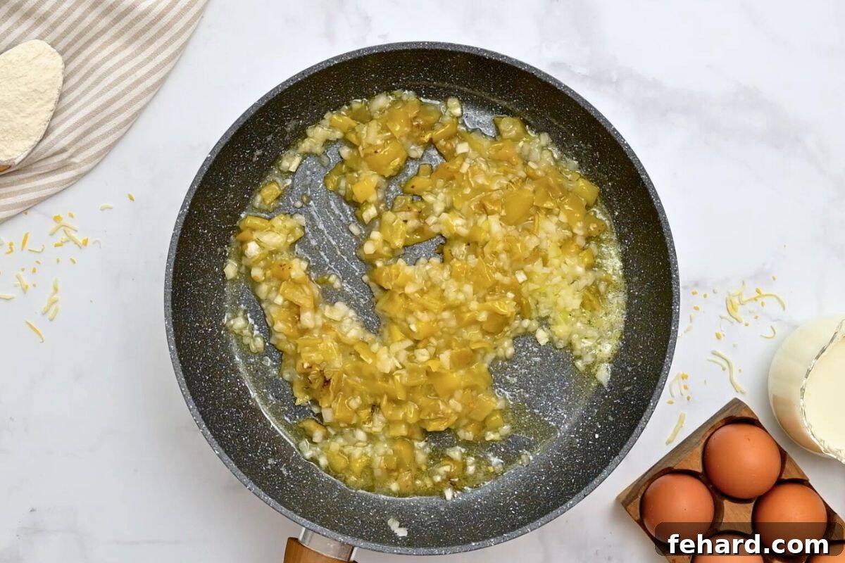 Minced onions and chopped mild green chiles being gently sautéed in melted butter within a gleaming skillet, creating an aromatic foundation for the casserole.