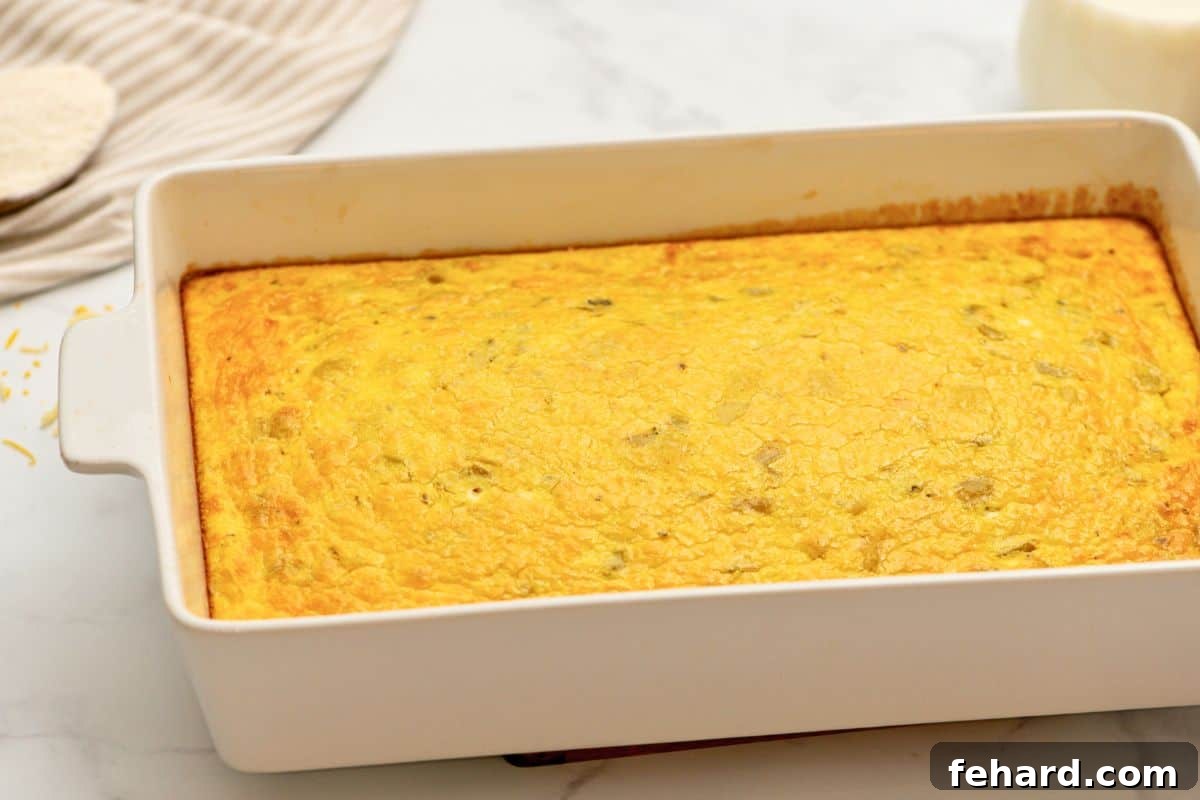 A beautifully baked green chile egg casserole, golden brown and puffed, cooling slightly in a white ceramic casserole dish after coming out of the oven.