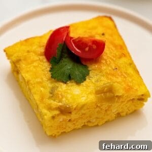 Slice of green chile egg casserole on white plate topped with diced tomatoes and cilantro.